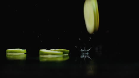 Rings-of-fresh-green-lime-sliced-fall-on-the-glass-with-splashes-of-water-in-slow-motion